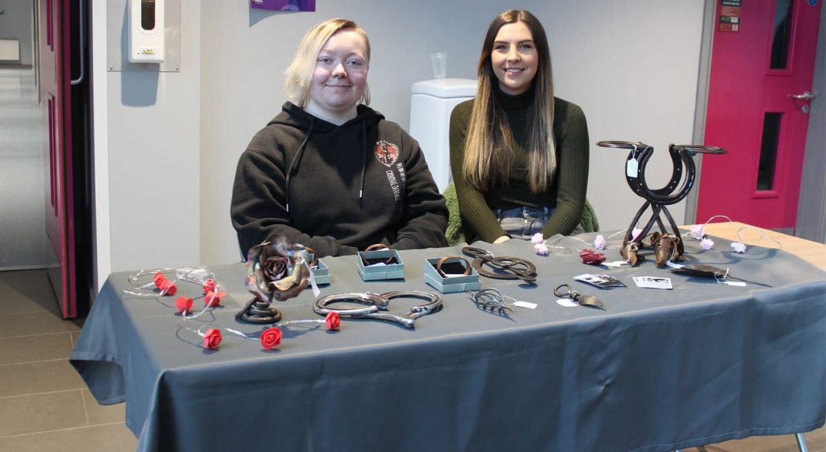 2 people sat behind a table displaying products for purchase